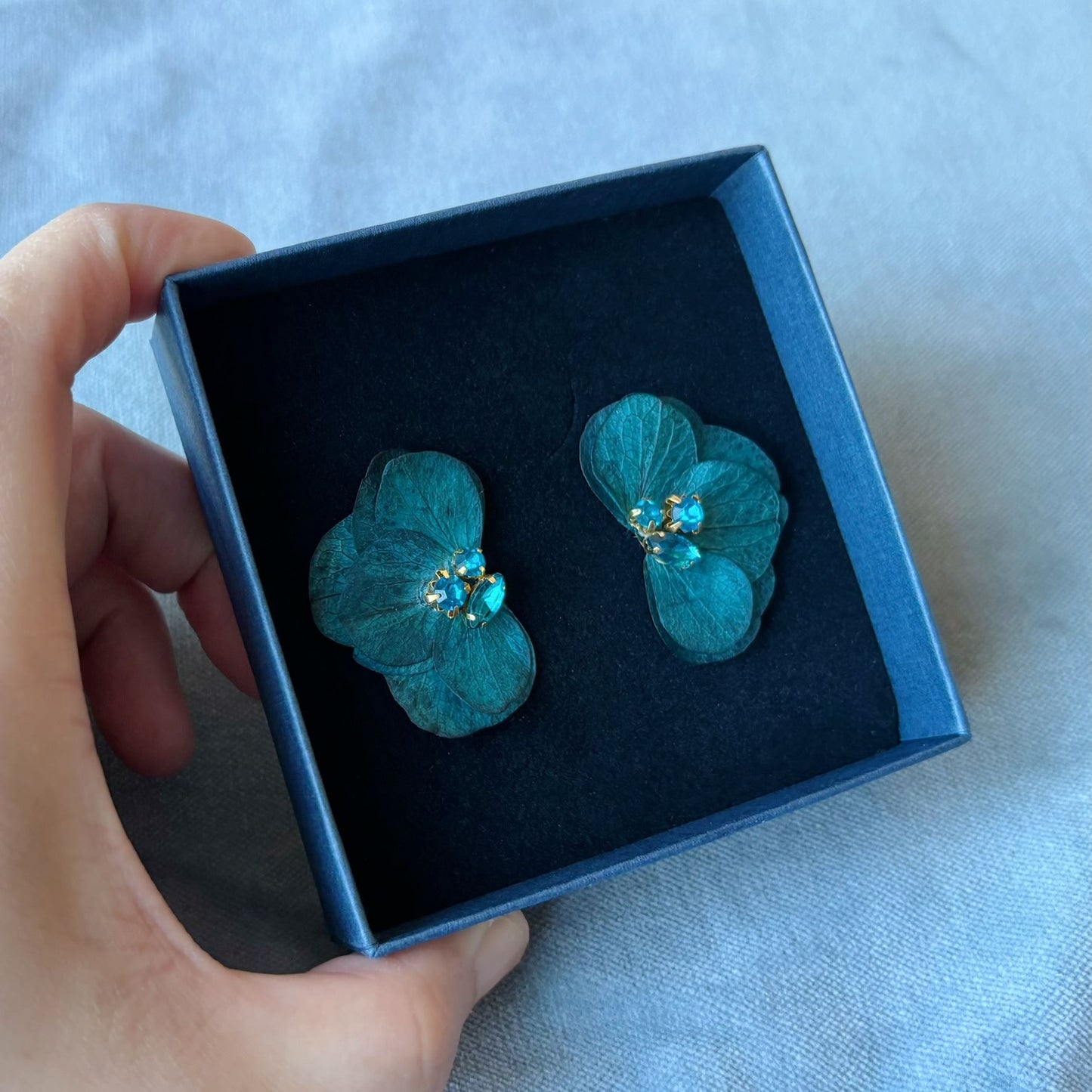 Parfaites pour un mariage ou une soirée, ces boucles d'oreilles Hana&Alice en hortensias bleu saphir et strass combinent naturel et élégance pour mariées ou témoins.