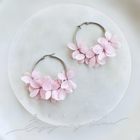 Boucles d'oreilles créoles avec hortensias stabilisés rose clair, idéales pour le mariage. Ces bijoux délicats sont parfaits pour la mariée, ses témoins ou ses demoiselles d’honneur. Leur design élégant et floral apportera une touche de raffinement et de fraîcheur à votre journée spéciale.