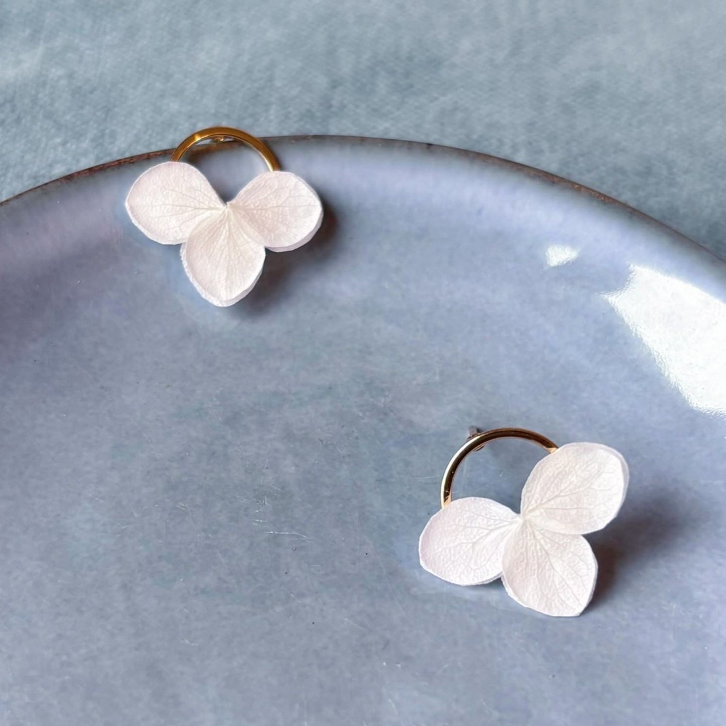 Bijoux de mariage dorés, puces d'oreilles ornées d'hortensias stabilisés pour une touche florale subtile.