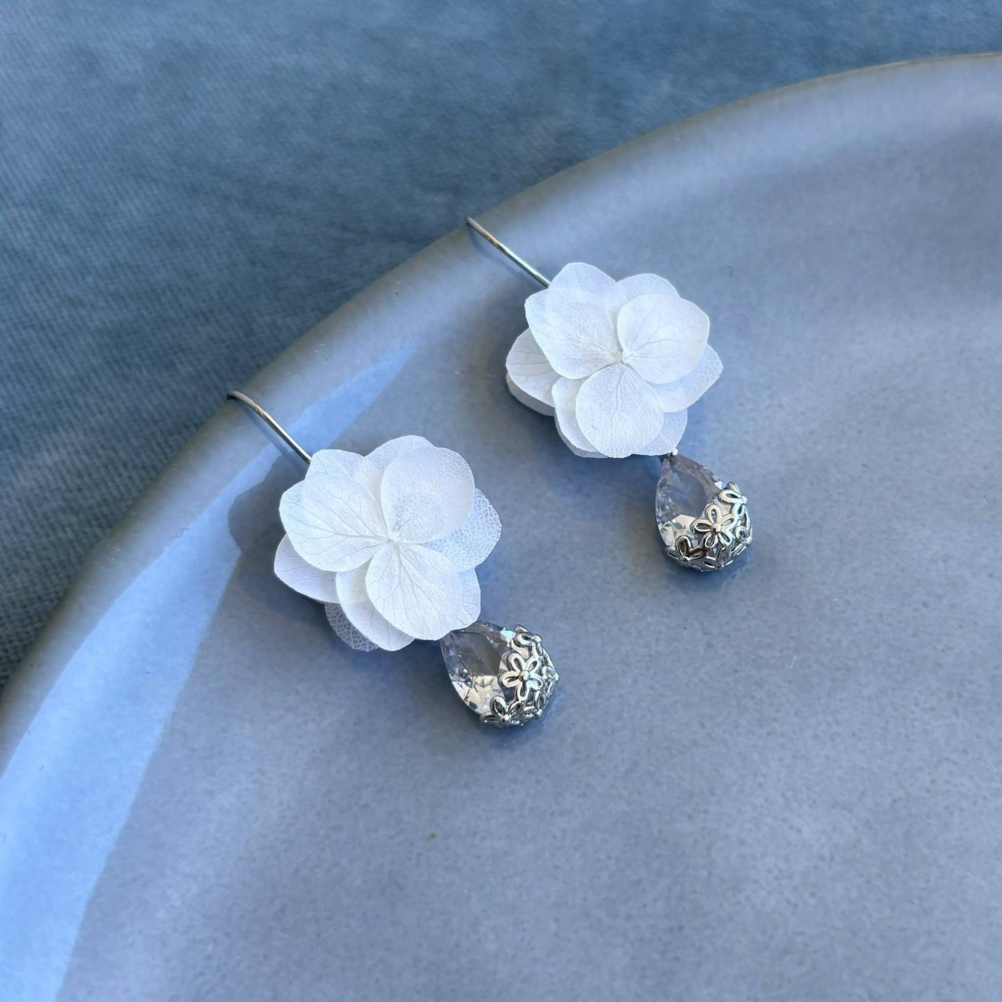 Accessoire mariage chic : boucles d'oreilles avec pétales d'hortensias blancs et perles cristallines, ajoutant une touche florale subtile à votre look.