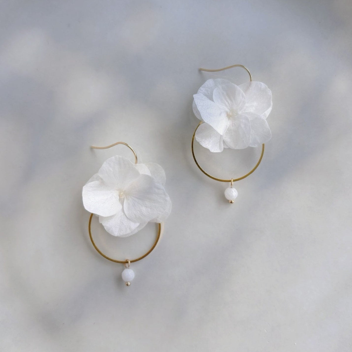 Boucles d'oreilles de mariage en créole avec fleurs d'hortensias stabilisés blancs et perle blanche, bijoux de mariage en fleurs pour apporter à votre tenue de mariage une touche naturelle et délicate, signés Hana&Alice.