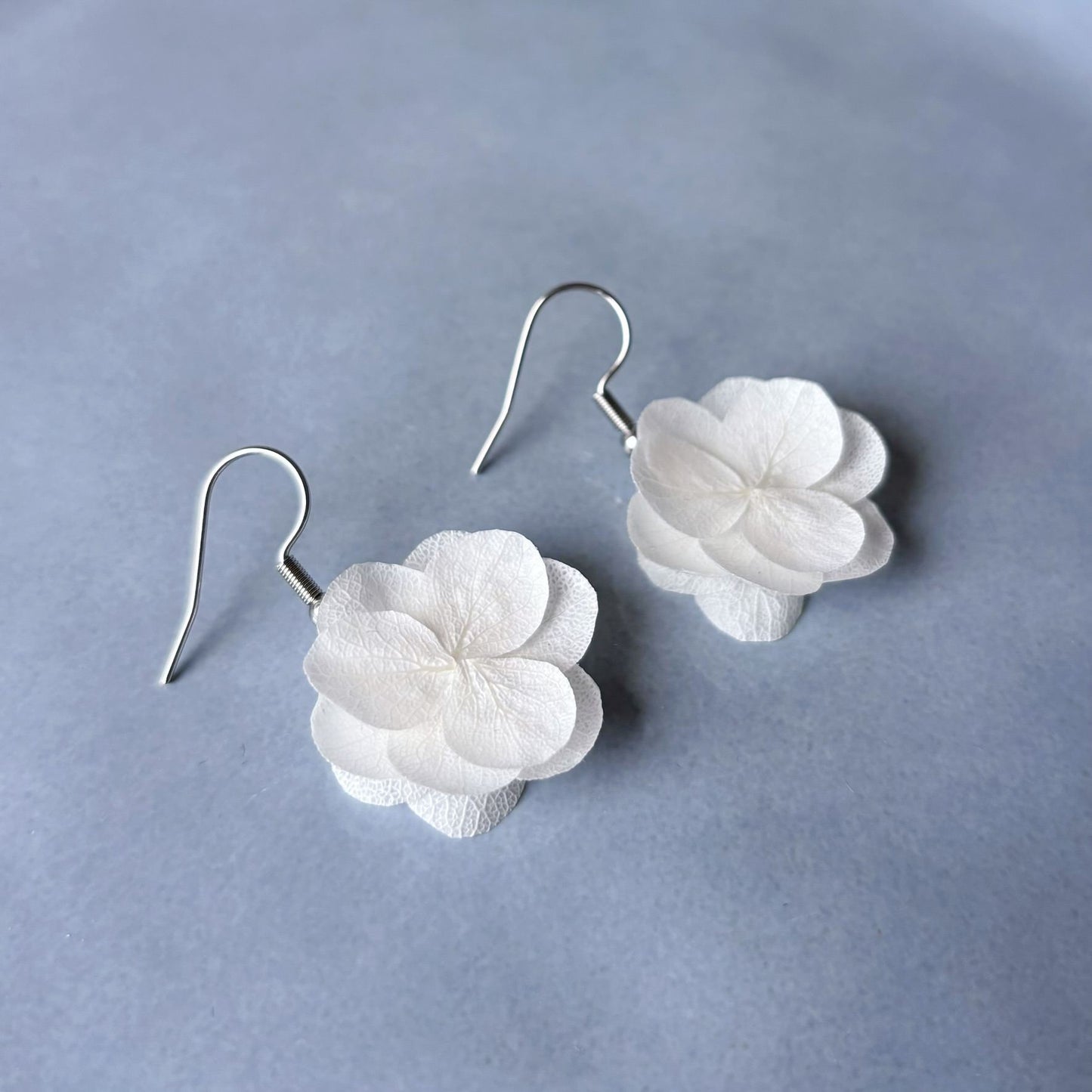Découvrez l'élégance intemporelle des boucles d'oreilles en hortensias stabilisés blancs crème. Un bijou délicat et unique, parfait pour ajouter une touche de grâce et d'originalité à votre mariage.
