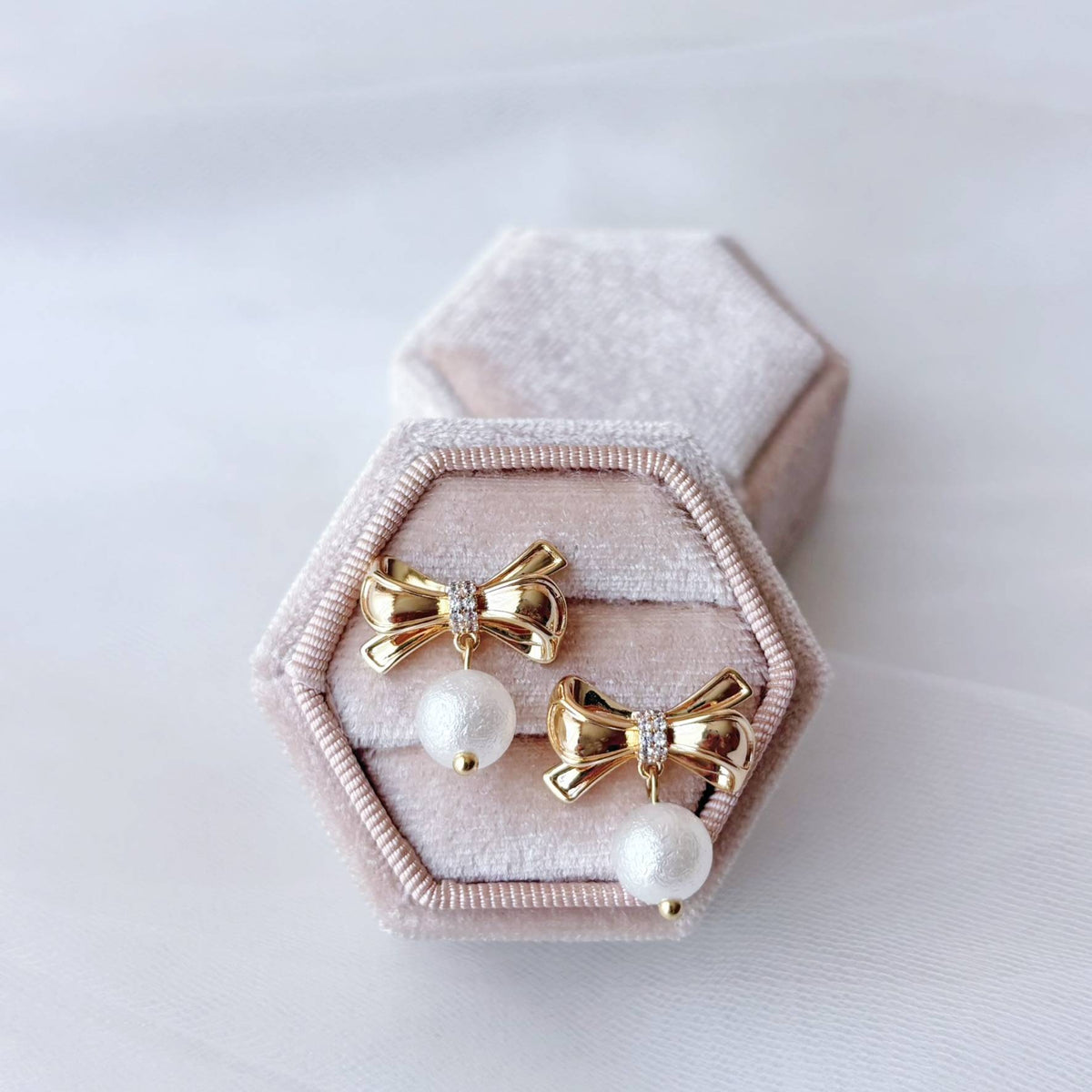 Boucles d’oreilles de fête avec délicat nœud doré et perle ronde lumineuse