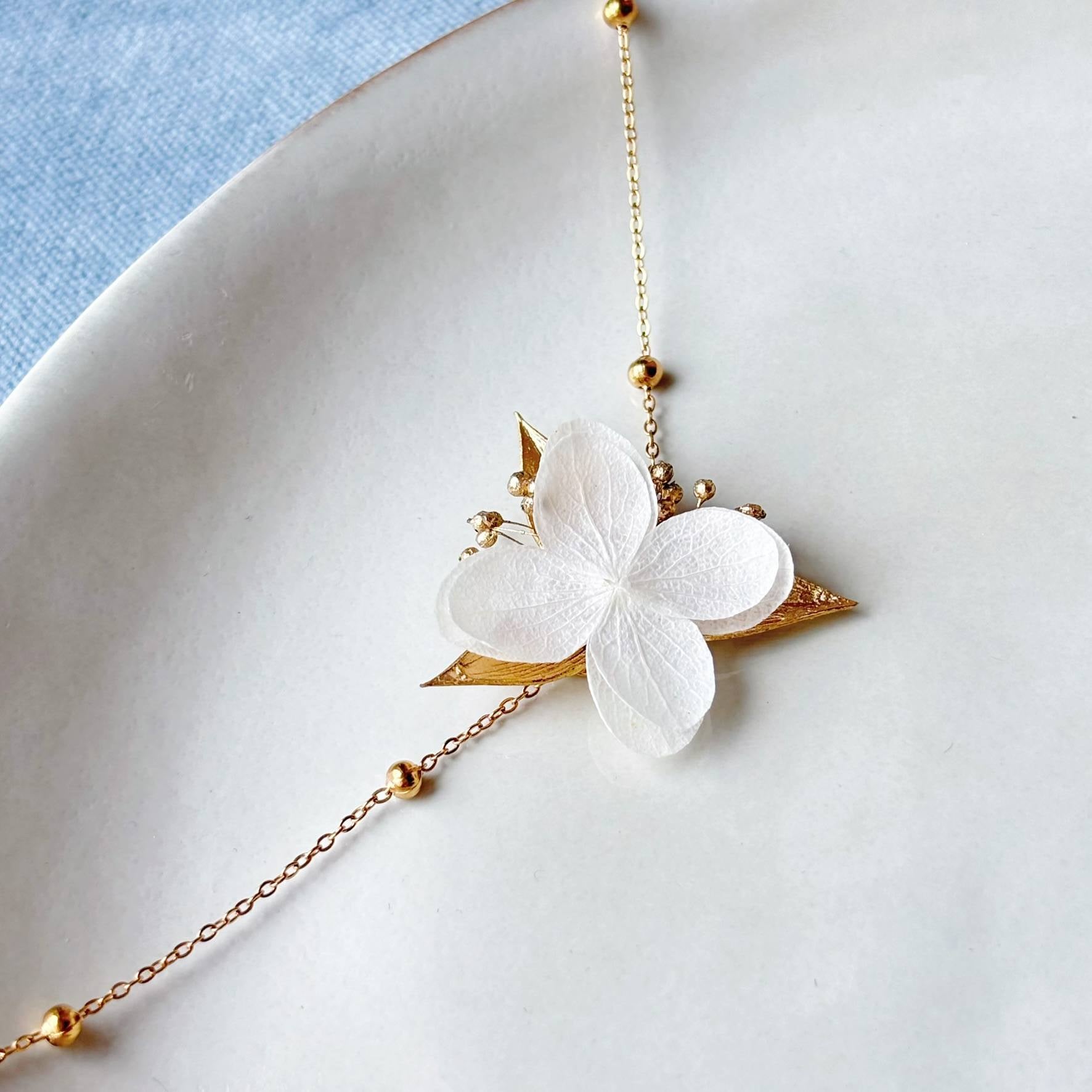 Bracelet floral blanc et doré pour parure de mariage, fleurs stabilisées et feuilles dorées.
